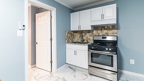 A kitchen with white cabinets, a tiled backsplash, a stainless steel stove, and a marble floor. - Boardwalk Hotel Charlee & Beach House Rentals (Seaside Heights)