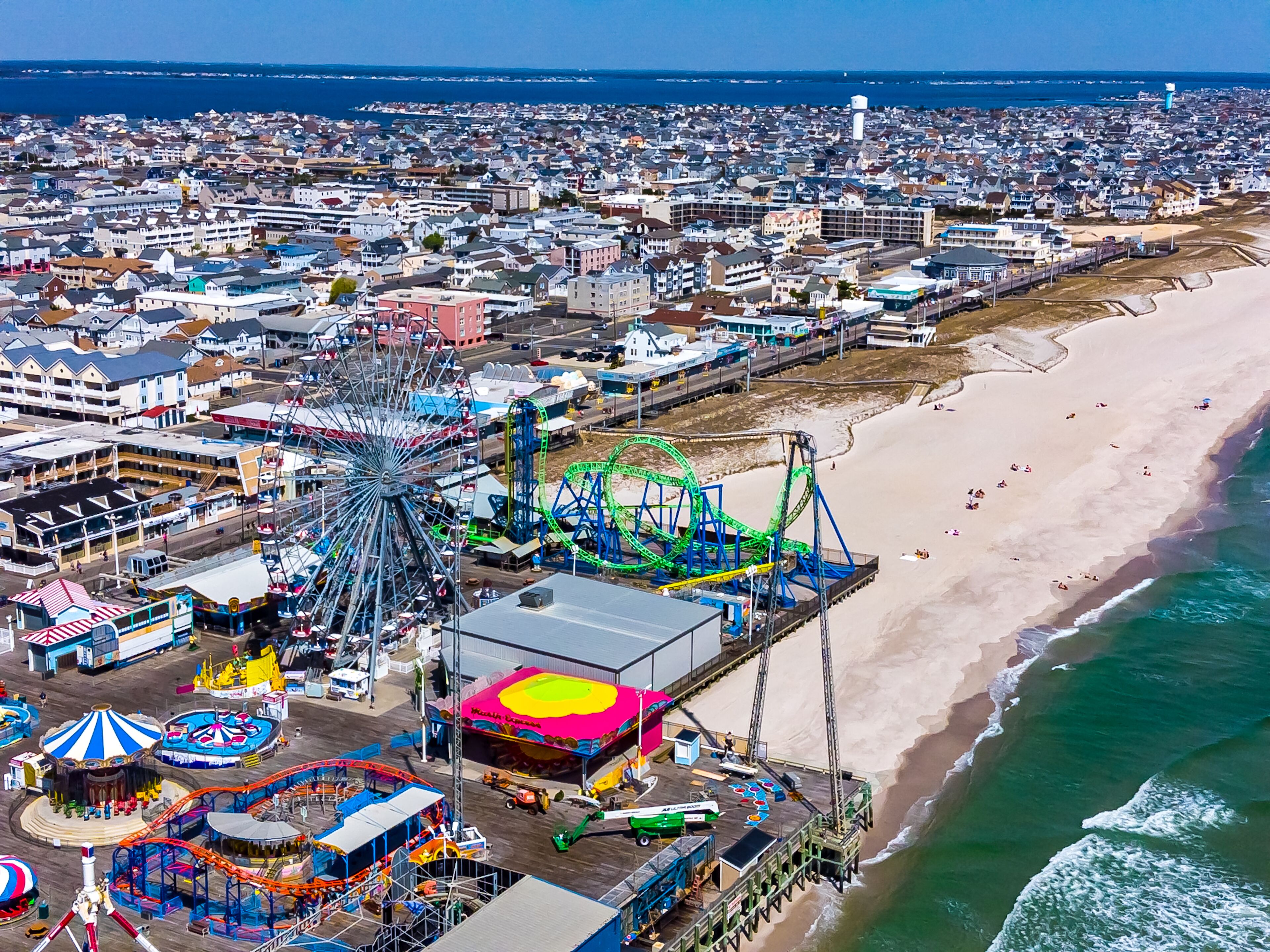 Vista aérea de un parque de atracciones costero con noria, montañas rusas y una playa.