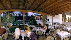 An outdoor dining area with tables and chairs, a covered roof, and a view of the surrounding landscape. - Irinna Hotel (Kefalonia)