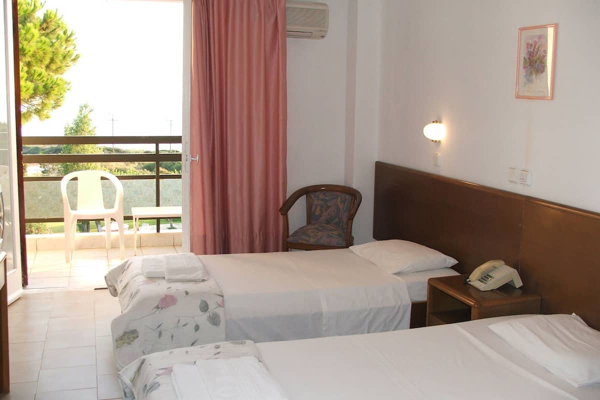 A hotel room with two beds, a chair, a phone, and a balcony with chairs.