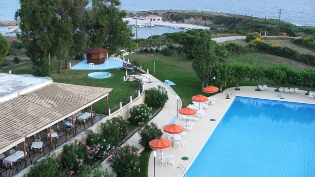 A swimming pool with lounge chairs and umbrellas, a patio area with tables and chairs, and a view of the sea. - Irinna Hotel (Kefalonia)