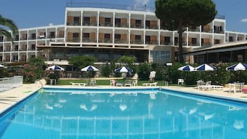 Relax by the hotel's large rectangular pool surrounded by lounge chairs and umbrellas, with trees and shrubs adding a touch of greenery.