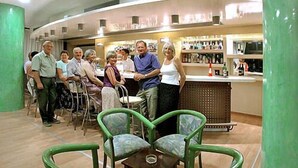 A group of people in a bar area with green chairs and a counter with bottles. - Irinna Hotel (Kefalonia)