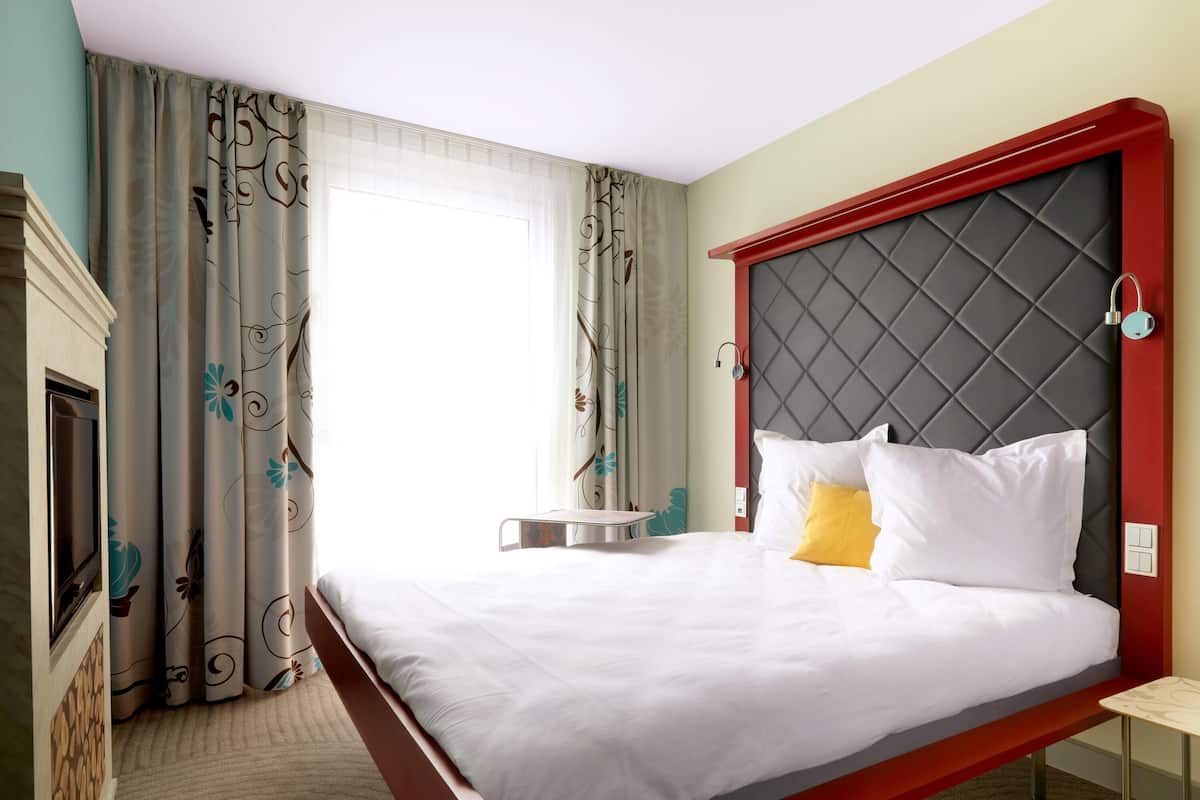 A hotel room with a bed, a bedside table, a chair, a small round table, and a fireplace.