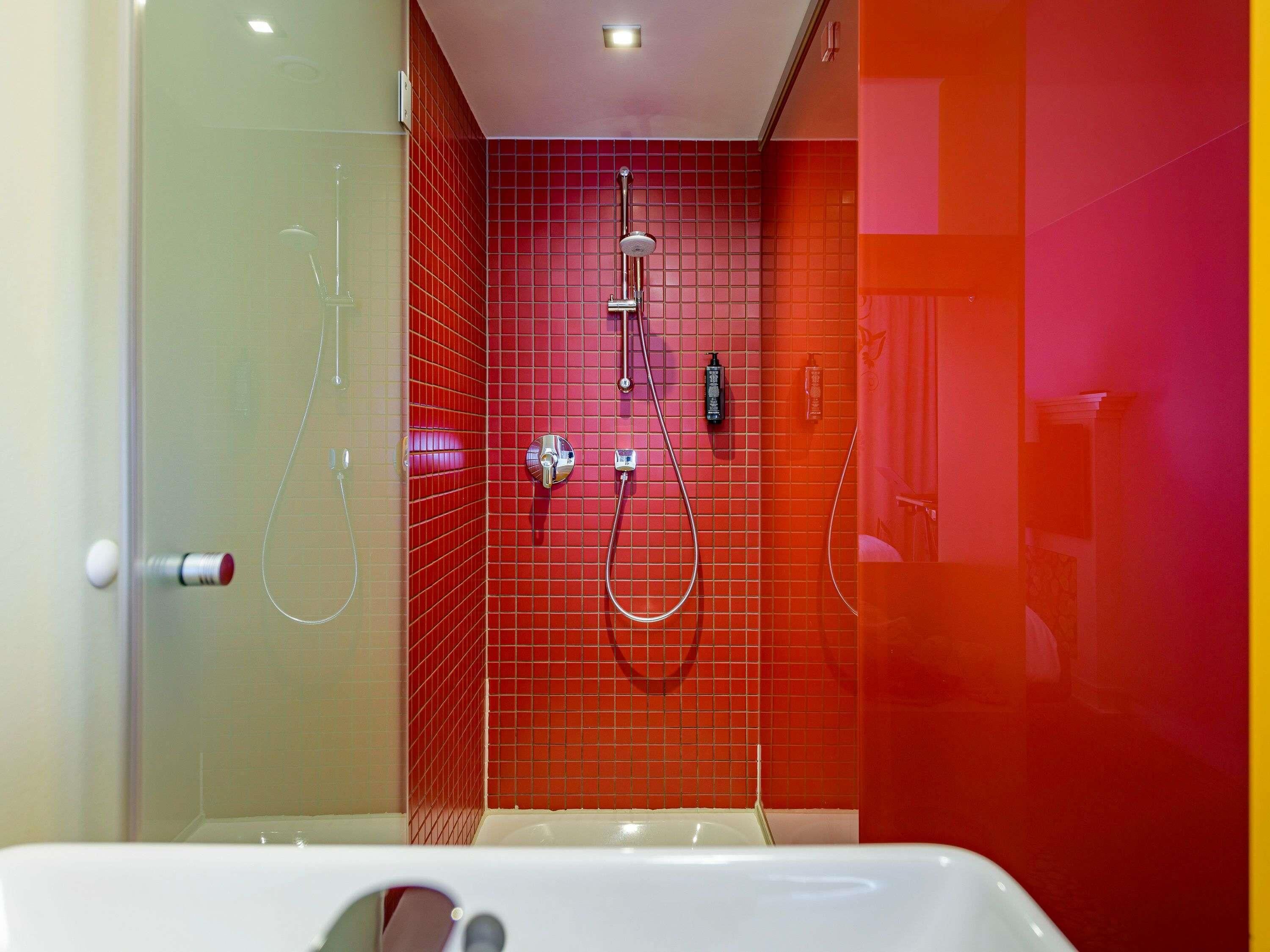 Une salle de bain moderne avec une douche à l’italienne en verre, une baignoire blanche et des murs recouverts de carreaux rouges.