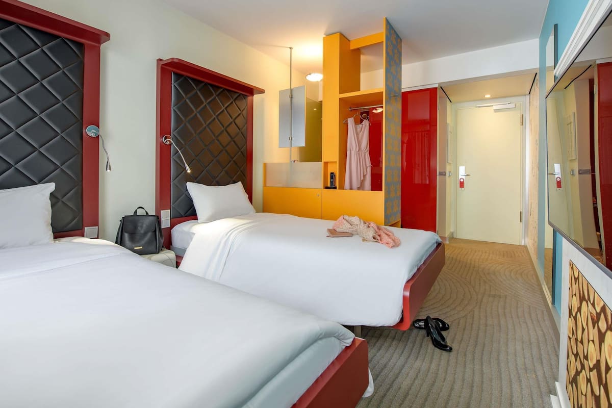 A hotel room with two beds, a red wardrobe, a mirror, and a red door.