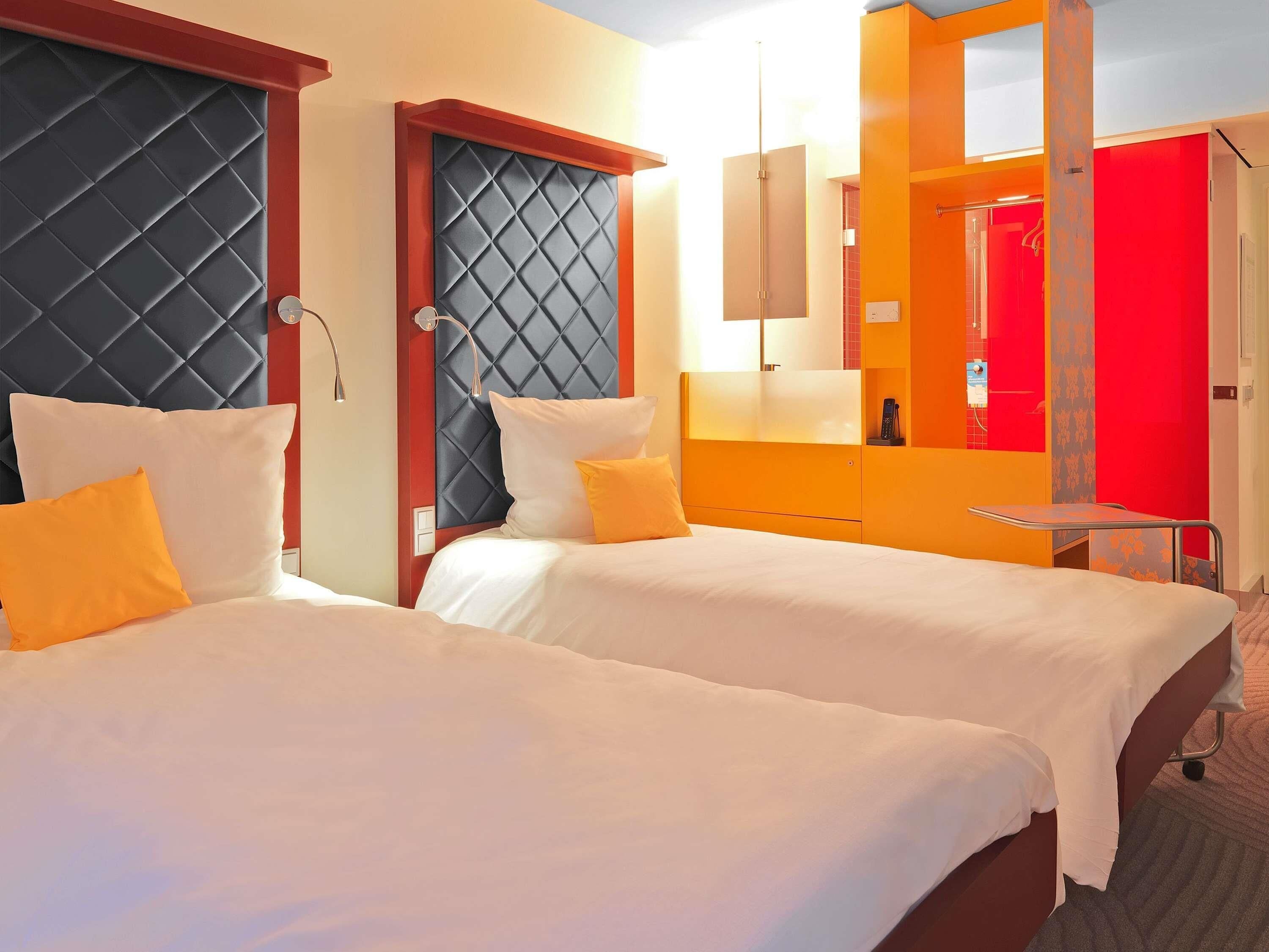 A hotel room with two beds, a red door, and a mirror.