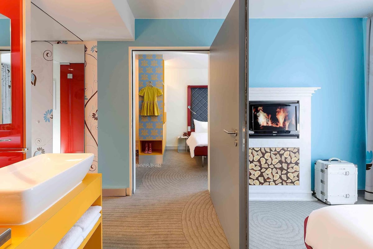 A hotel room with a bed, a TV mounted on the wall, a fireplace, and a wardrobe.