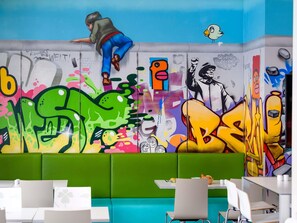 A vibrant graffiti wall, a green cushioned seating area, and a table with a white tablecloth. - ibis Styles Hotel Berlin Mitte (Berlin)