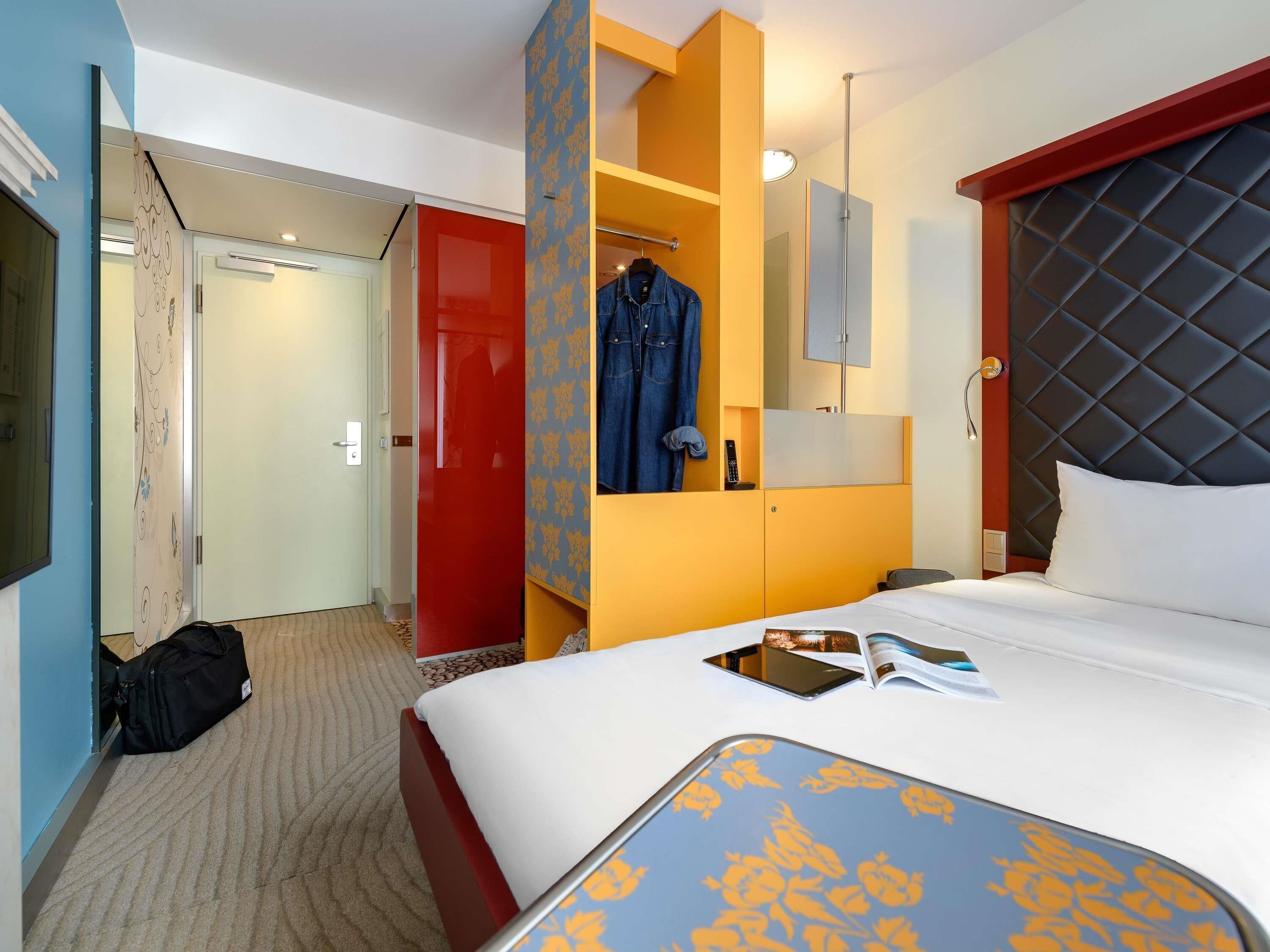 A hotel room with a bed, a wardrobe, a mirror, and a door leading to another room.