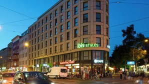 Un hotel de varios pisos con la señalización 'Ibis Styles', una cafetería y un restaurante 'Back Factory'.