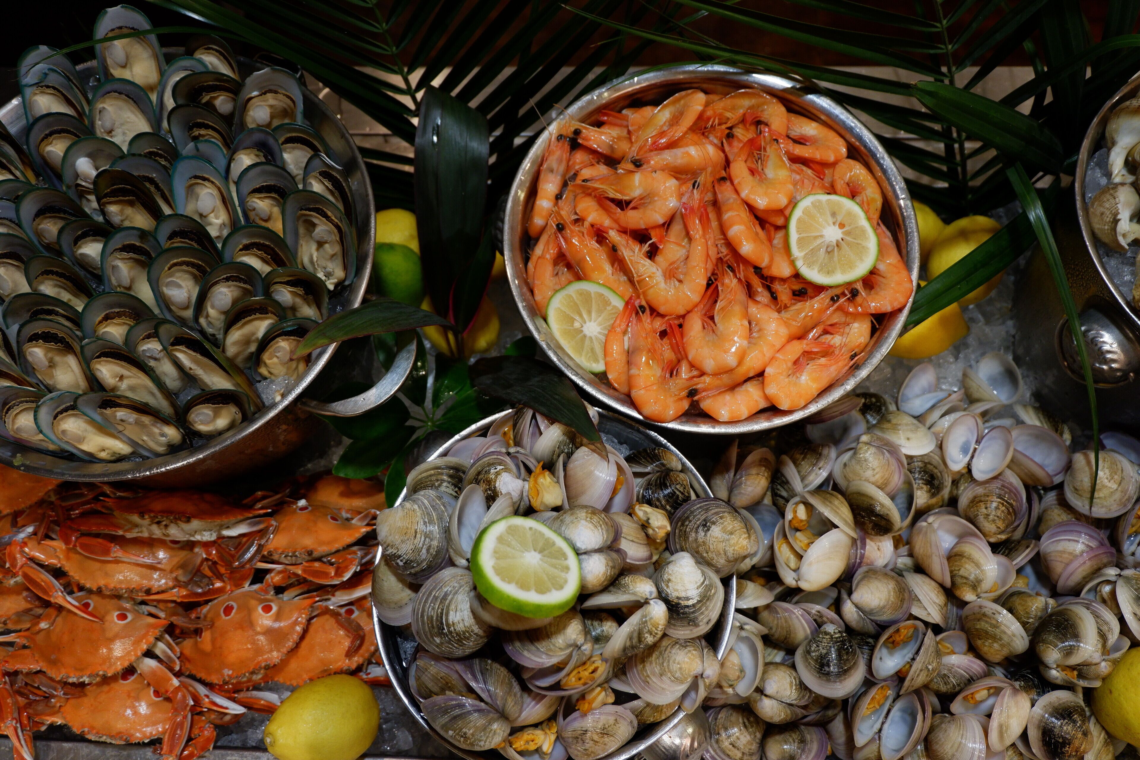 A variety of seafood including shrimp, clams, and crabs, arranged on a metal tray with lime wedges.