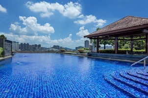 A swimming pool with a tiled deck, a covered seating area, and a view of high-rise buildings in the background.