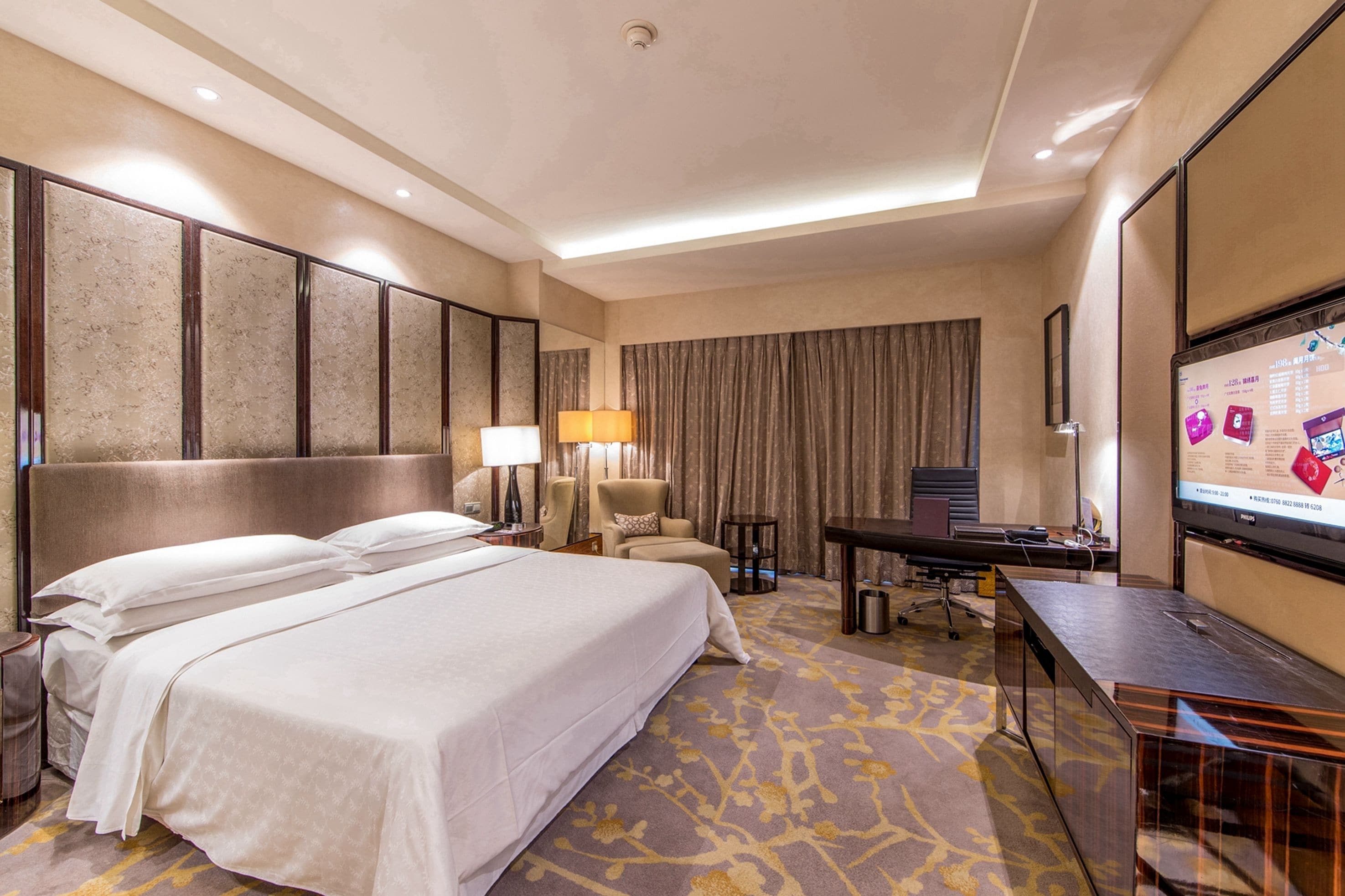 Une chambre d’hôtel avec un grand lit, un bureau avec un ordinateur, une télévision et un coin salon comprenant une chaise et une lampe.