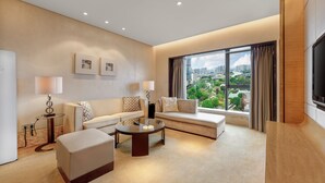 A modern living room with a sofa, ottoman, coffee table, and a large window offering a city view. - Sheraton Zhongshan Hotel (Zhongshan)