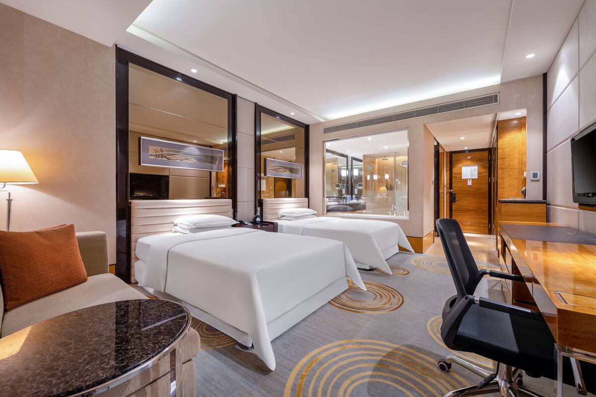 Habitación de hotel con dos camas, un escritorio, una silla, un televisor y una lámpara.