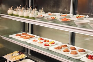 Un bufé con diversos alimentos, entre ellos frutas, quesos y platos de carne.