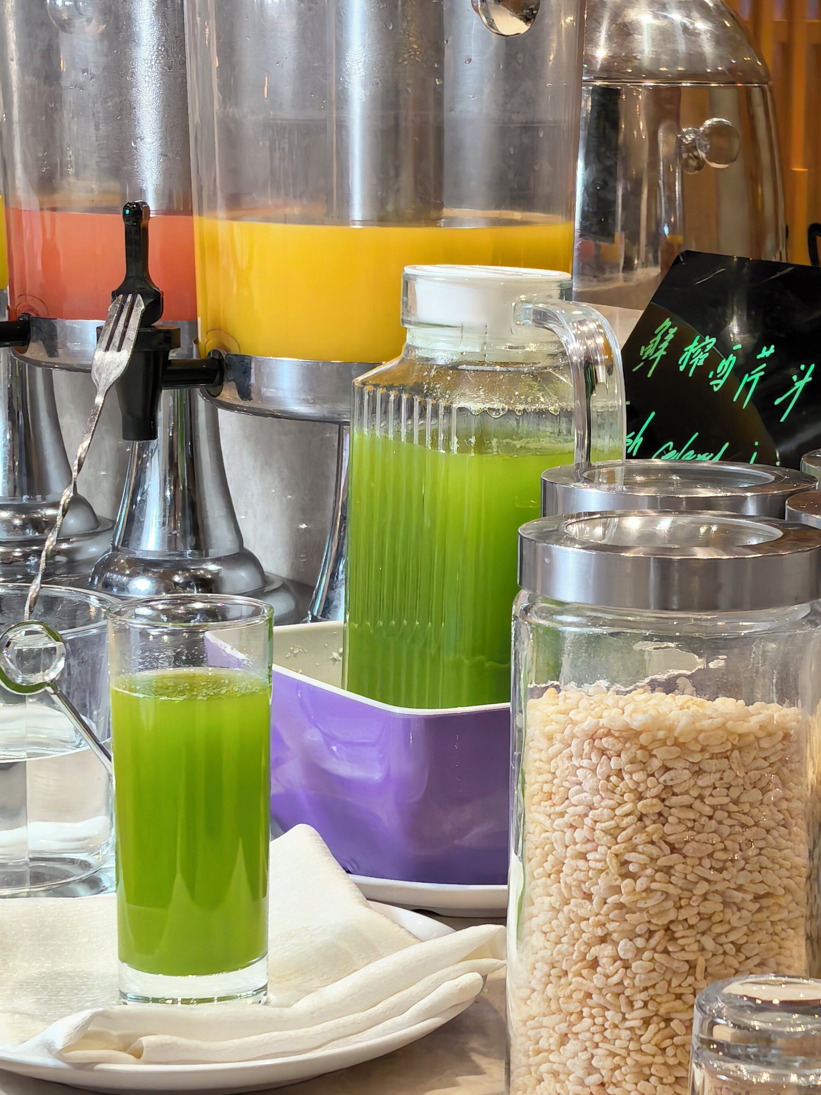 Variedad de recipientes de comida y bebida, entre ellos una jarra de vidrio, un vaso con líquido verde y un frasco lleno de granos.
