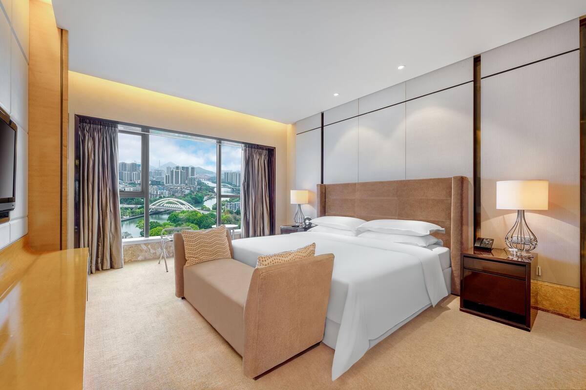 Una habitación de hotel moderna con una cama grande, un sofá, un escritorio y vistas a la ciudad.
