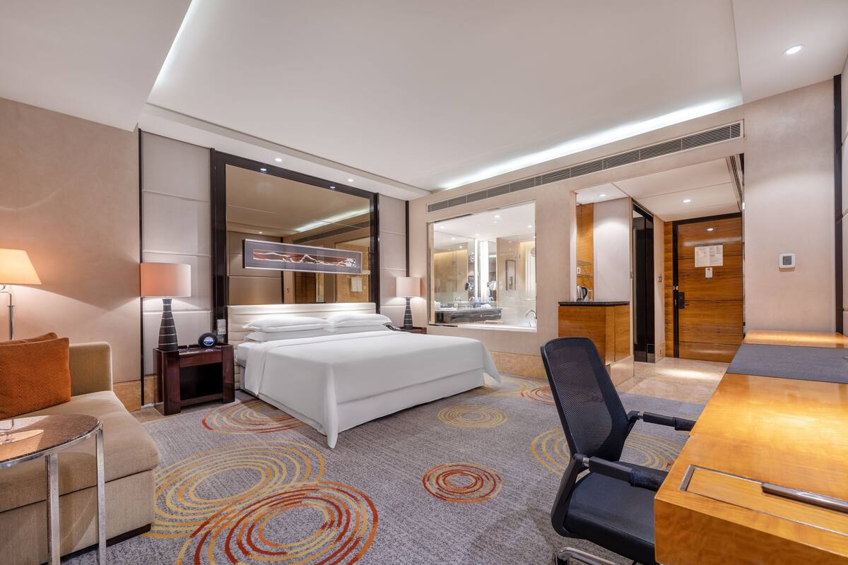 Una habitación de hotel con cama, escritorio, silla, lámpara y espejo.