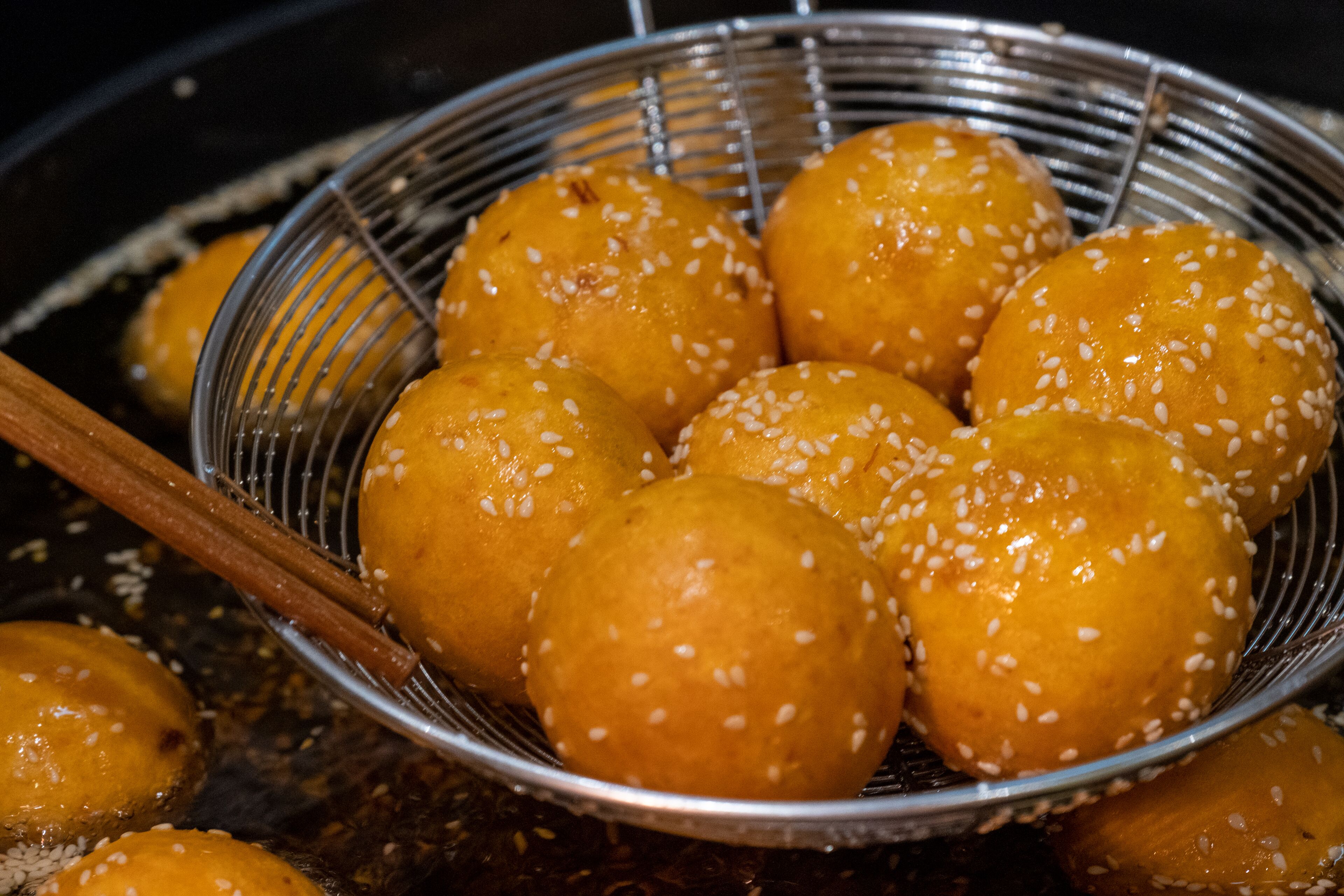 A basket of round, golden-brown items sprinkled with white sesame seeds, likely fried dough or pastries, resting on a metal surface.