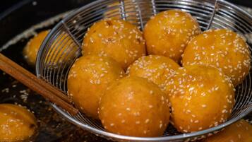 A basket of round, golden-brown items sprinkled with white sesame seeds, likely fried dough or pastries, resting on a metal surface.