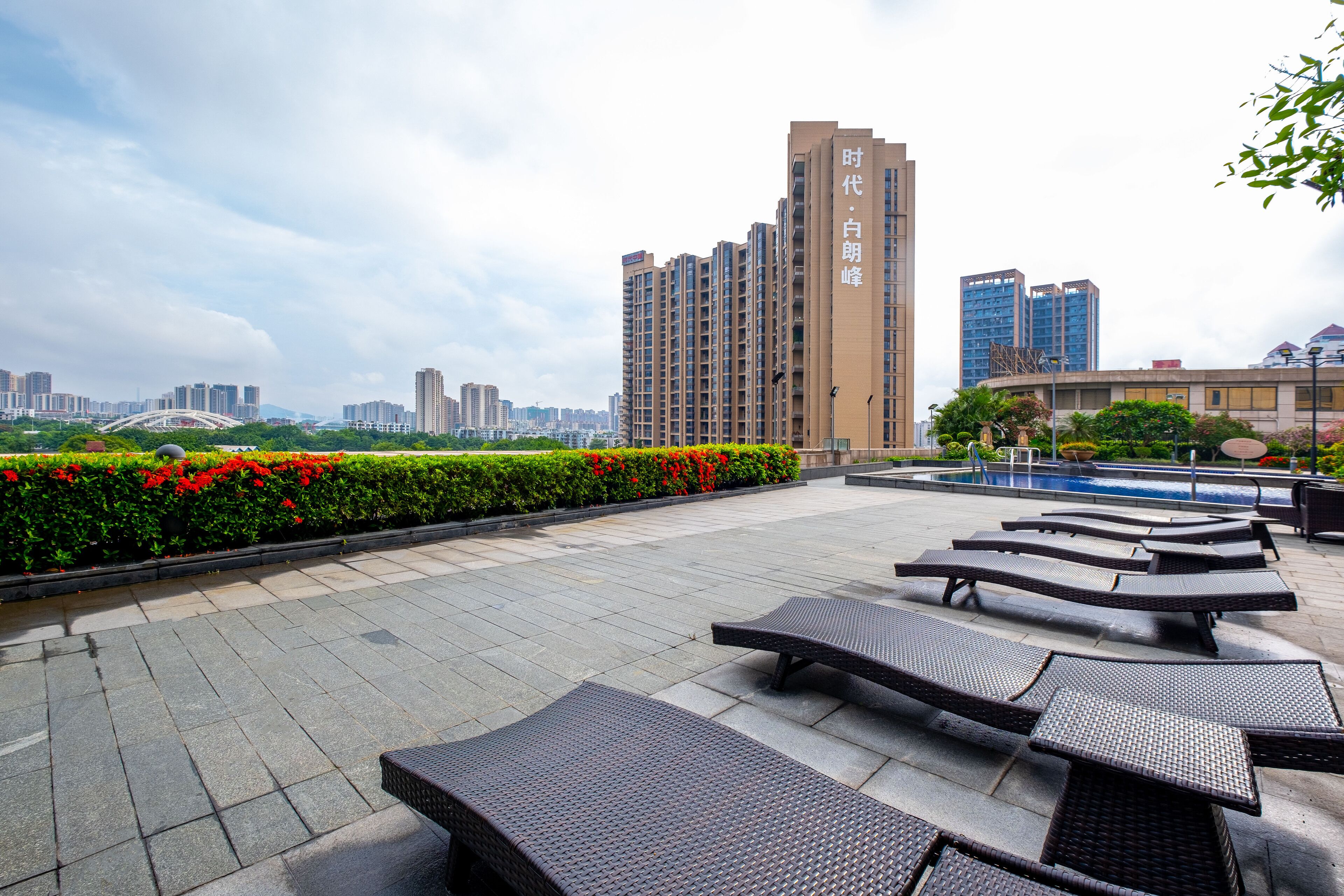 A rooftop terrace with lounge chairs, a swimming pool, and a cityscape view.