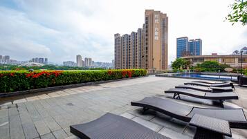 A rooftop terrace with lounge chairs, a swimming pool, and a cityscape view.
