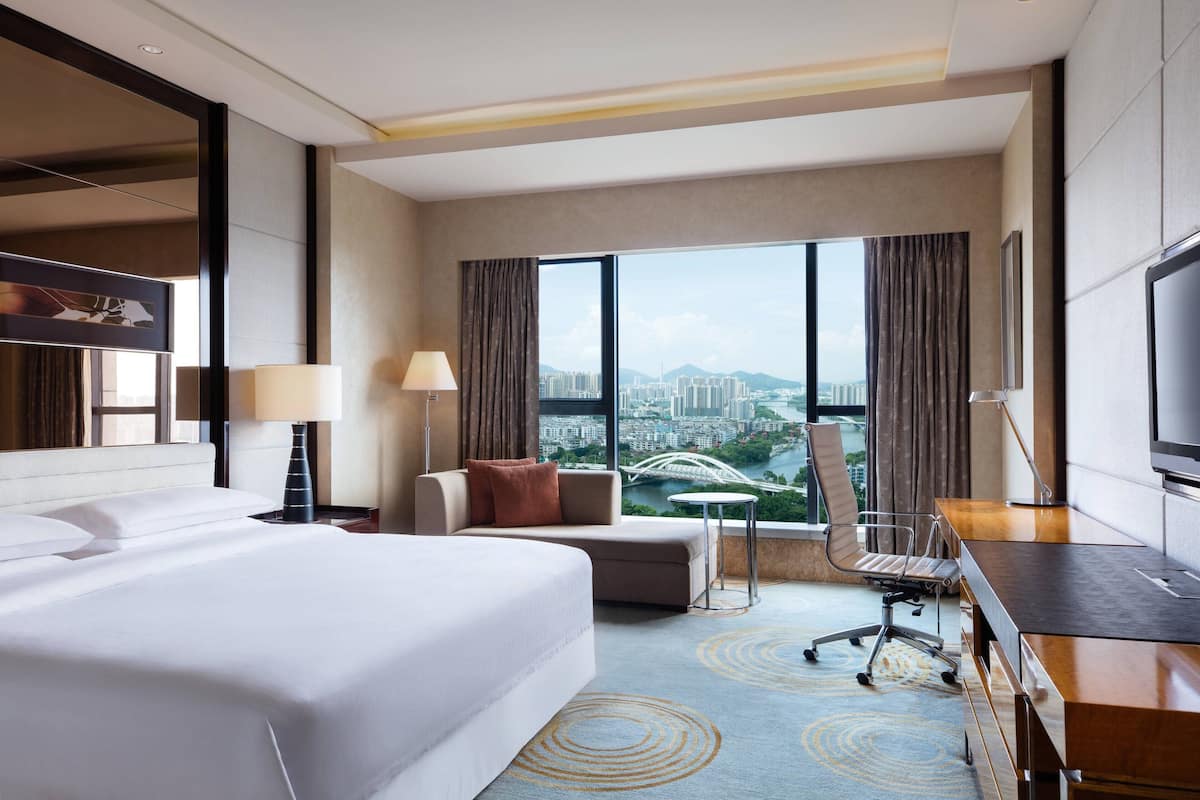 Habitación de hotel con una cama grande, un escritorio, una silla y vistas a la ciudad.