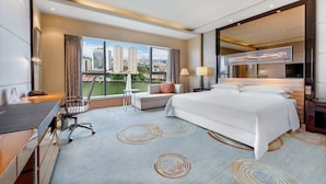 A modern hotel room with a large bed, a desk, a chair, and a view of the cityscape through large windows. - Sheraton Zhongshan Hotel (Zhongshan)