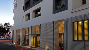 A modern hotel with multiple floors, large windows, and a well-lit entrance. - Airotel Patras Smart (Patras)
