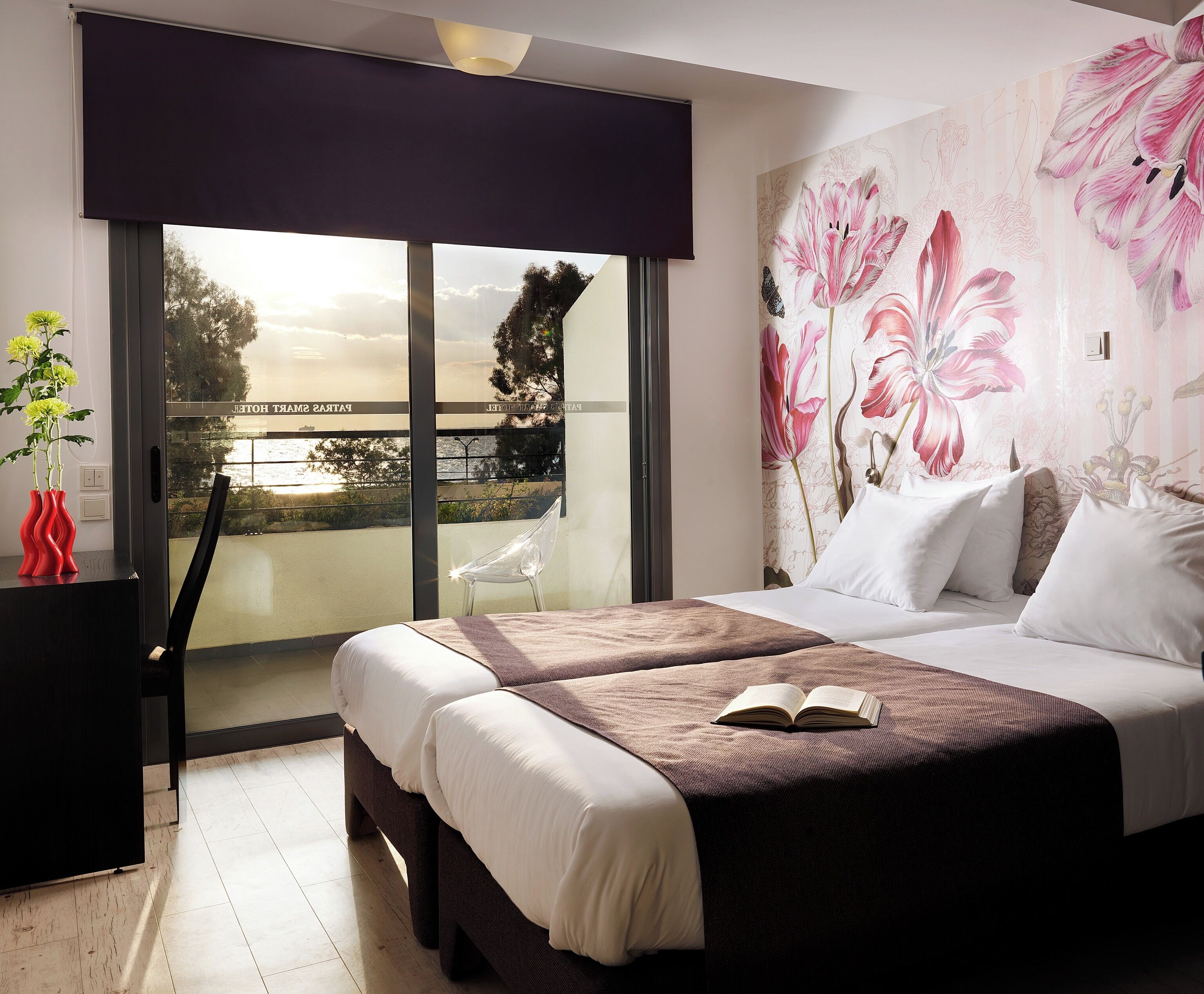 Una habitación de hotel con una cama, una silla, una mesa con un florero y vistas a un puente.