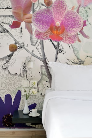 A bedroom with a bed, a nightstand with a vase and a cup, and a wall with a floral pattern. - Patras Smart Hotel, Vassilicos House of Hospitality (Patras)