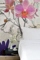 Un dormitorio con una cama, una mesita de noche con un florero y una taza, y una pared con estampado floral.