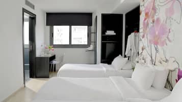 Habitación de hotel con dos camas, un escritorio con silla, una ventana y un baño visible a través de una puerta abierta.