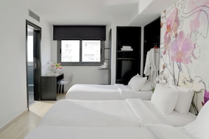 Habitación de hotel con dos camas, un escritorio con silla, una ventana y un baño visible a través de una puerta abierta.