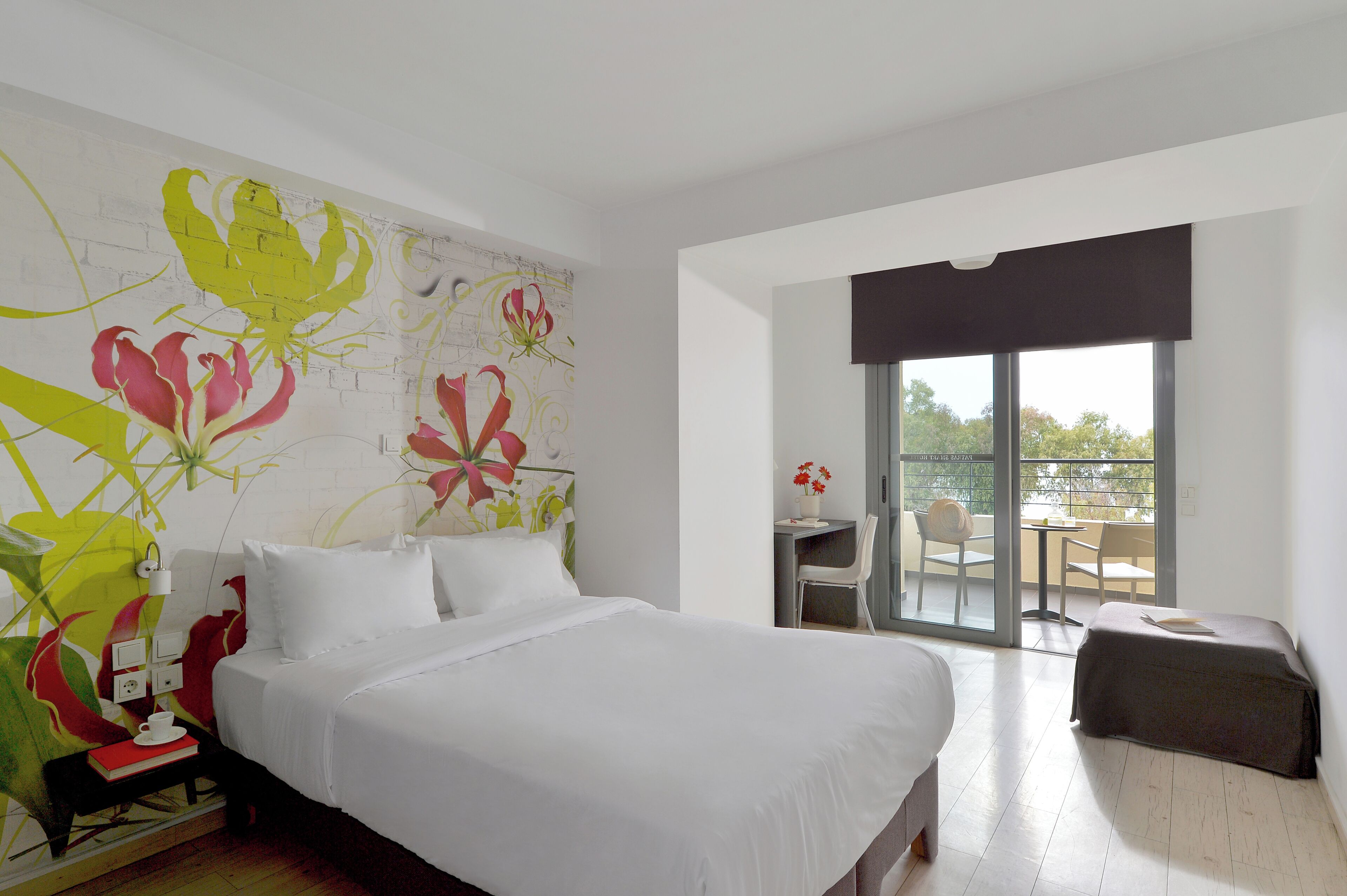 A hotel room with a large bed, a desk with a chair, and a balcony with a table and chairs.