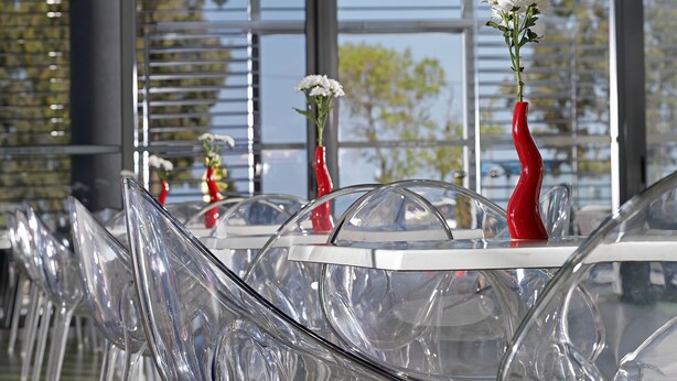 A row of transparent chairs with a green carpet, white tables, and red vases with flowers. - Airotel Patras Smart (Patras)