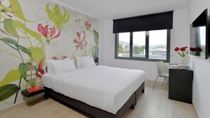 A bedroom with a large bed, a nightstand, a desk, a chair, a window with a view, and a wall with a floral mural.
