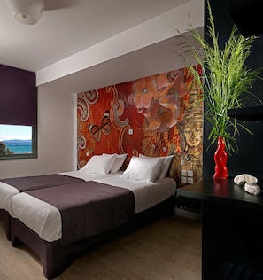A modern bedroom with a large bed, a decorative wall tapestry, and a view of the sea through a window. - Patras Smart Hotel, Vassilicos House of Hospitality (Patras)