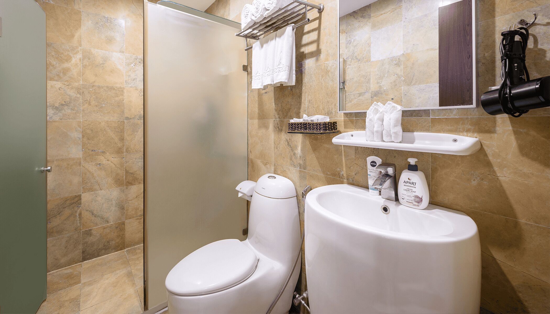 Casa de banho com sanita, lavatório e chuveiro. Existem toalhas e artigos de higiene pessoal no lavatório.
