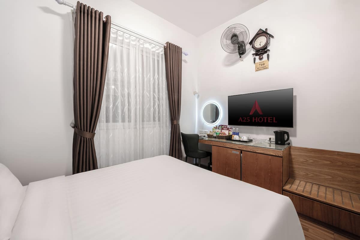 A hotel room with a bed, a desk with a computer, a TV, and a clock on the wall.