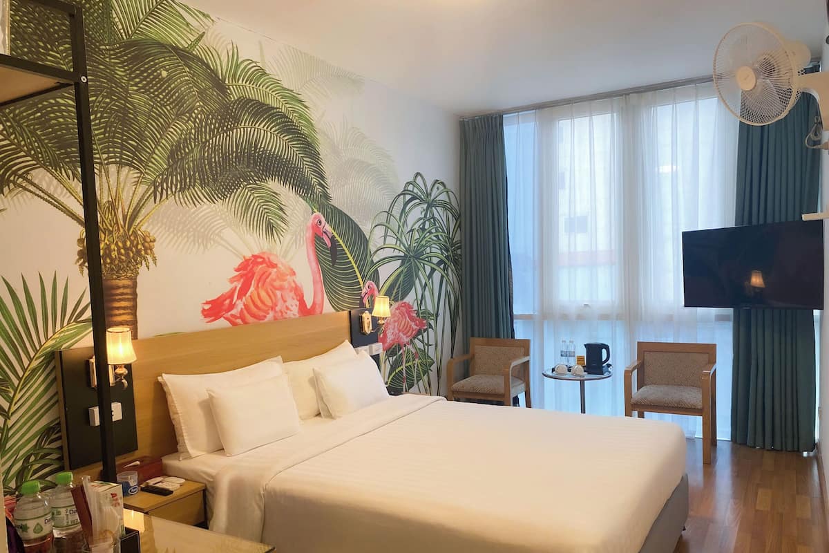A hotel room with a large bed, a TV, a desk with a lamp, a chair, and a small table with a coffee pot.