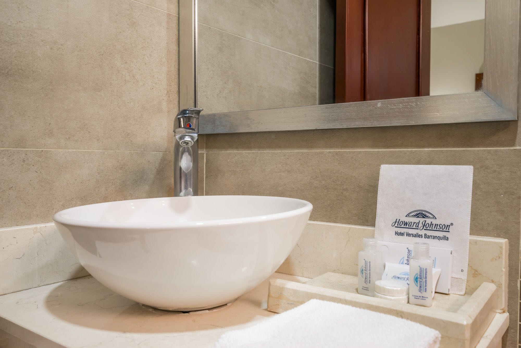 A white vessel sink with a chrome faucet, a mirror above, and toiletries on a wooden tray.