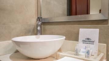A white vessel sink with a chrome faucet, a mirror above, and toiletries on a wooden tray.