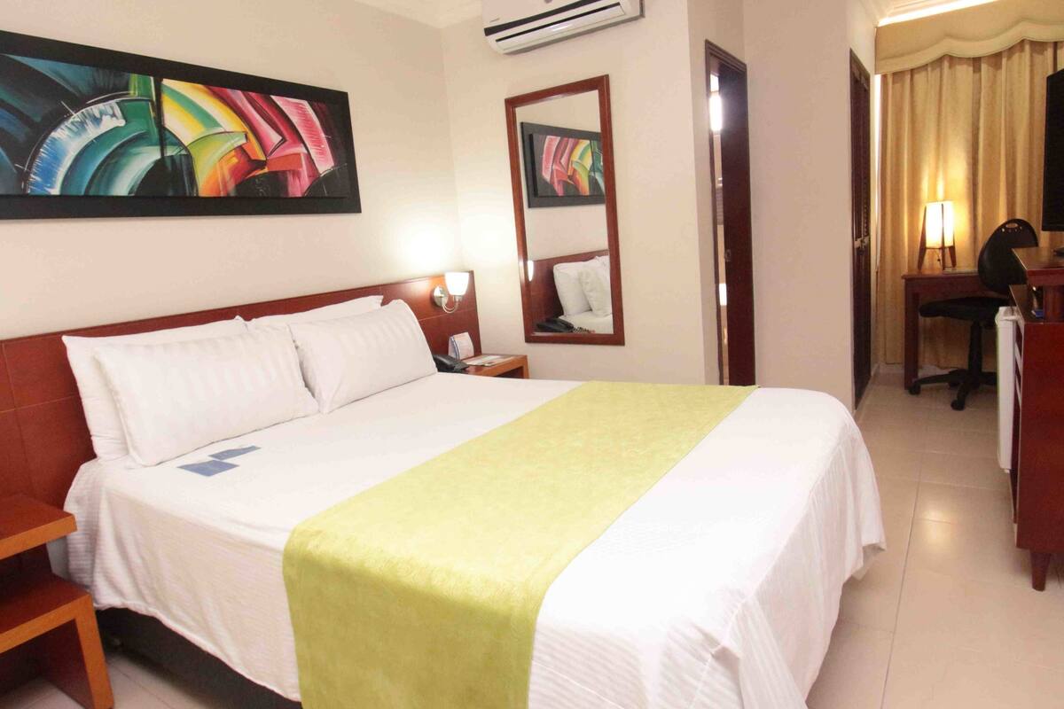 Ein Hotelzimmer mit Bett, Schreibtisch, Sessel, Fernseher und Bildern an der Wand.