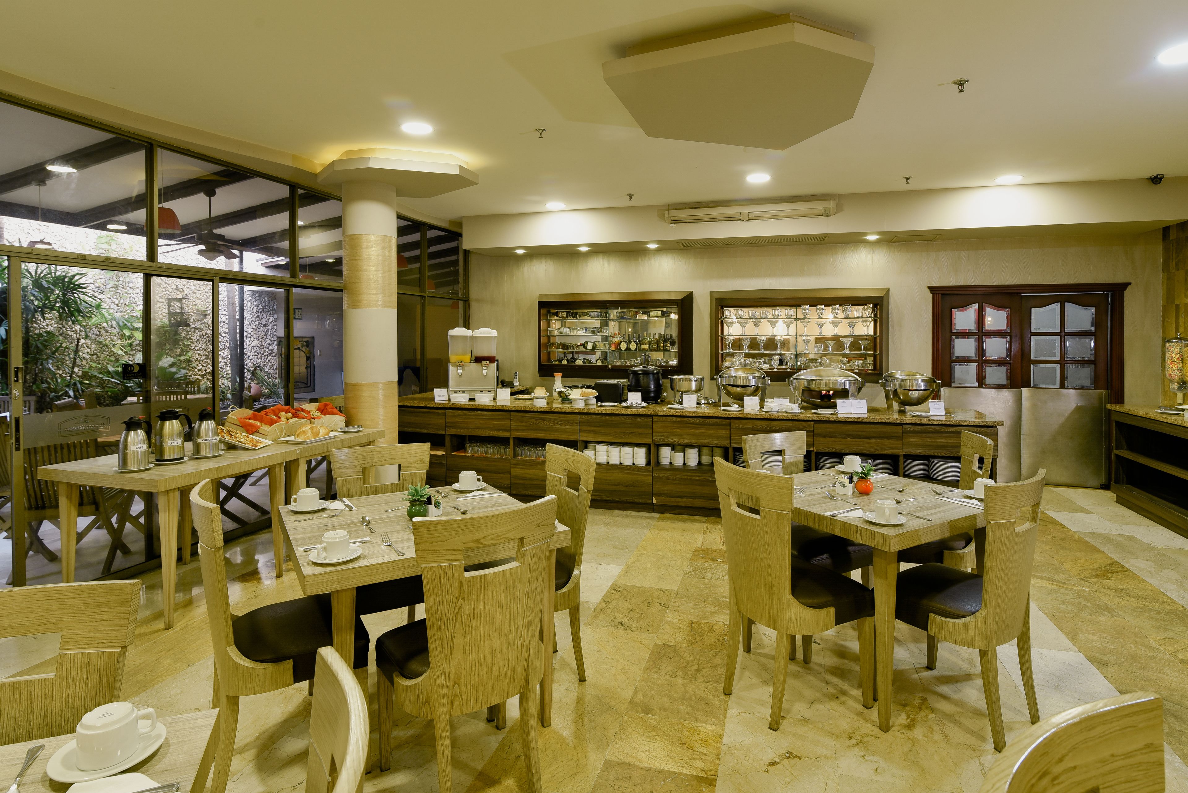 Un restaurante con mesas y sillas de madera, una zona de bar con estantes llenos de botellas y vistas amplias a través de grandes ventanales.