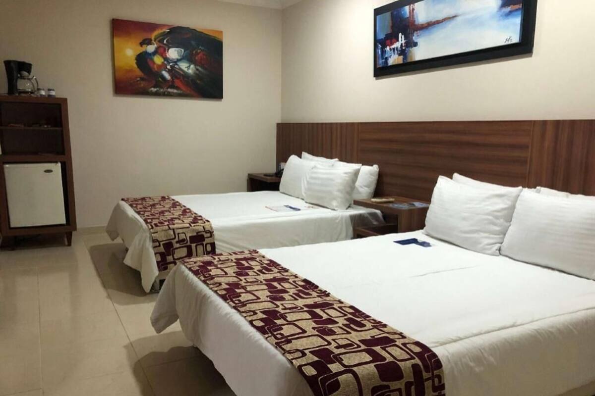 Ein Hotelzimmer mit zwei Betten, einem Holzkopfteil, einem kleinen Schrank und Bildern an den Wänden.