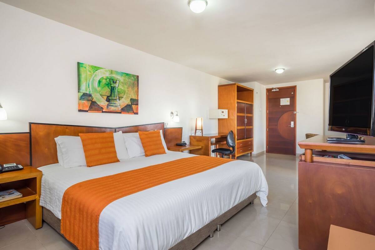 Ein Hotelzimmer mit einem großen Bett, einem Schreibtisch, einem Fernseher und einem Kleiderschrank.