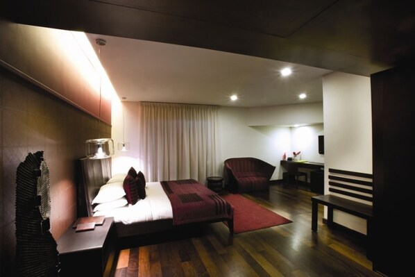 A modern hotel room with a bed, bedside table, lamp, chair, and a small desk with a chair. - The Park Pod (Chennai)
